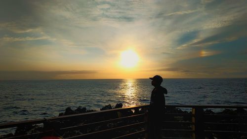 Silhouette man looking at sea against sky during sunset