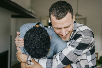 Smiling man hugging friend in kitchen