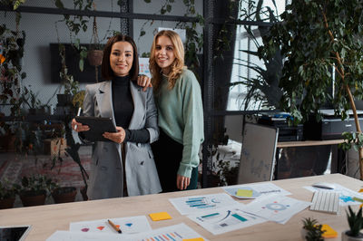 Two millennial women looking at camera confidently and posing in office during break