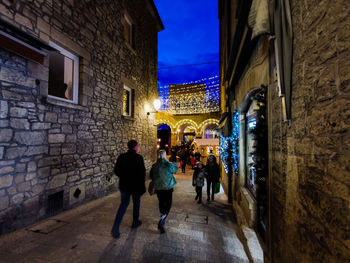 People walking in alley amidst buildings at night