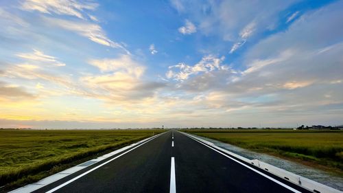 Road passing through land against sky during sunset