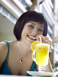 Close-up portrait of smiling mid adult woman having drink at sidewalk cafe