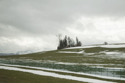 Scenic view of grassy field with snow against cloudy sky