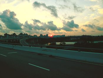 Vehicles on road against sky during sunset in city