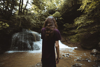 Rear view of woman standing by waterfall in forest