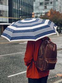 Rear view of man standing on wet street holding an umbrella