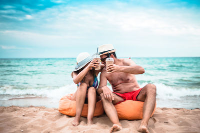 Couple having drink at beach against sky