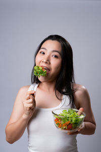 Portrait of young woman holding food against white background