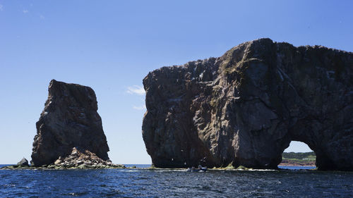 Rock formation by sea against clear sky