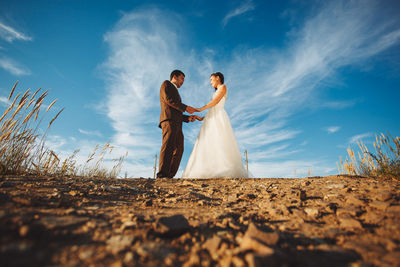 Full length of bride and bridegroom standing at beach against sky