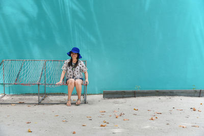 Full length of woman sitting on bench against wall