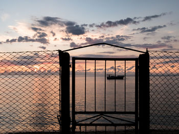 Silhouette gate by sea against sky during sunset
