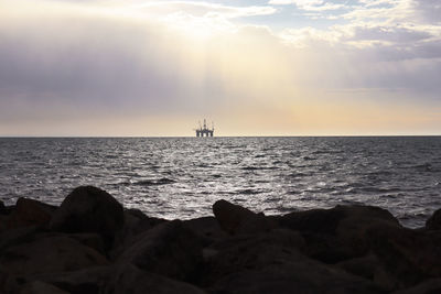 Oil rig in ocean viewed over rocks at dawn