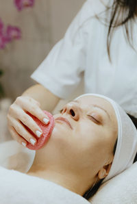 A girl cosmetologist cleanses the patient s face with a scrubbing sponge.