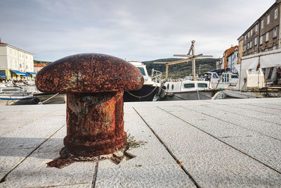 Metallic structure on footpath by street against sky in city