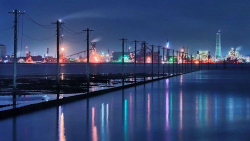 Illuminated bridge over river against sky at night