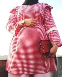 Midsection of woman holding umbrella while standing against pink background