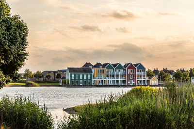 Colorful houses by river against cloudy sky during sunset