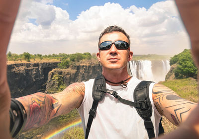 Portrait of man wearing sunglasses against waterfall