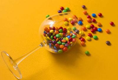 Colorful candies in a wine glass on yellow background