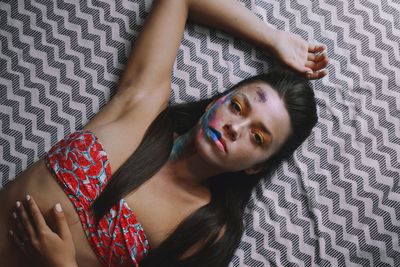 High angle portrait of woman with face paint lying on bed