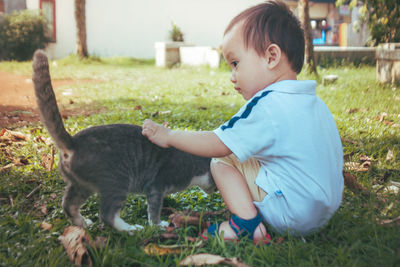 A baby boy touching a cat in garden