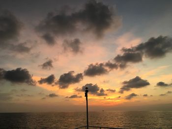 Silhouette street light by sea against sky during sunset