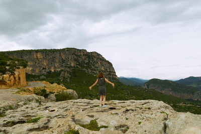 Rear view of woman standing with arms outstretched on cliff against mountains