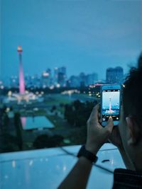 Cropped image of man photographing illuminated national monument in city at dusk