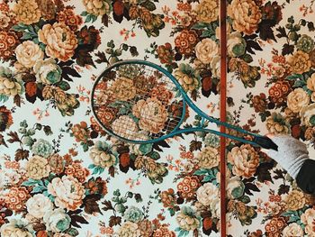 Cropped hand holding racket by floral pattern wall
