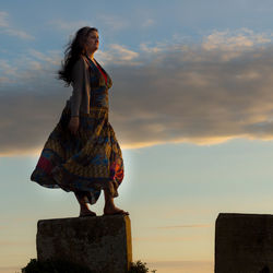 Low angle view of woman standing against sky during sunset