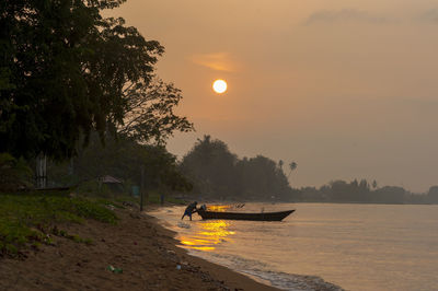 Silhouette fisherman with boat on shore at beach against sky during sunset