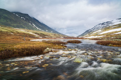 Scenic view of river flowing by mountain against sky