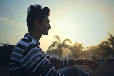 Side view of young man looking away against sky during sunset