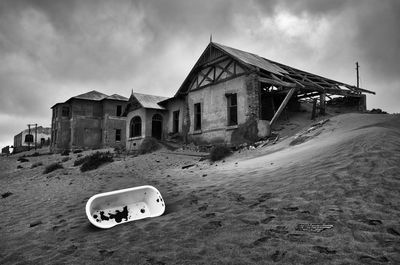 Abandoned bathtub on sand by hut against sky