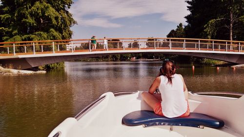 Rear view of woman sailing on boat in river by footbridge