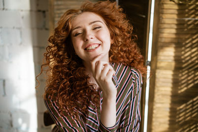 Portrait of happy redhead young woman near window