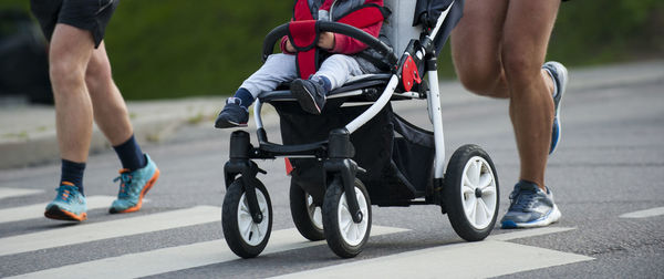 Low section of man with baby in stroller running on road during marathon