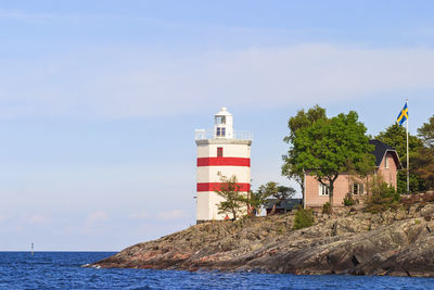 Lighthouse by sea against building against sky