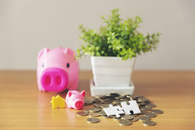 Close-up of coins with model homes and piggy banks on wooden table against wall