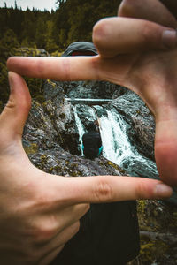 Cropped image of man making finger frame against waterfall
