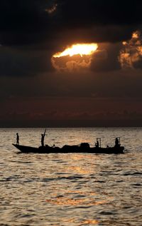 Silhouette people in fishing boat on sea during sunset