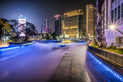 Illuminated modern buildings by street against sky at night