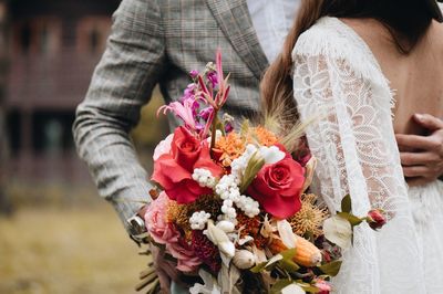 Midsection of couple holding bouquet while standing outdoors