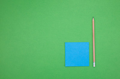Directly above shot of pencil and adhesive note against green background