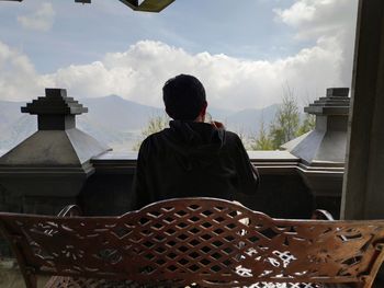 Rear view of man standing by building against sky