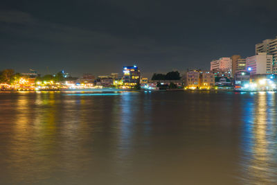 Illuminated city by river against sky at night