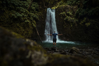 Man standing on rock against waterfall in forest