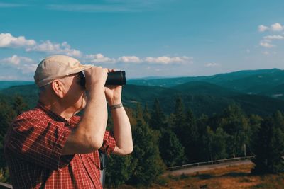 Midsection of man photographing on mobile phone against mountains