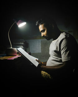 Side view of man reading book at night